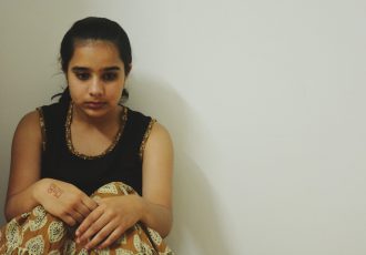 depressed-teenager-girl-looking-down-while-sitting-by-white-wall