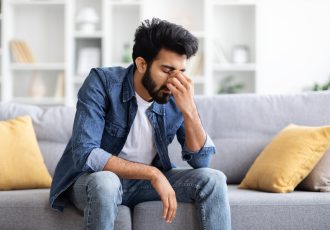 Seasonal Depression. Portrait Of Sad Young Indian Man Sitting On Couch At Home, Upset Tired Eastern Guy Resting In Living Room, Suffering Life Problems Or Mental Breakdown, Copy Space