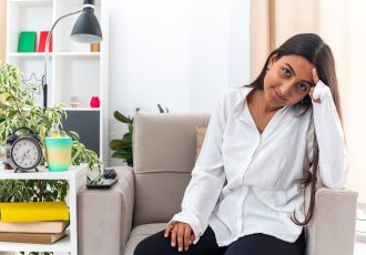 young girl in white shirt and black pants looking at camera happy and positive smiling sitting on the chair in light living room